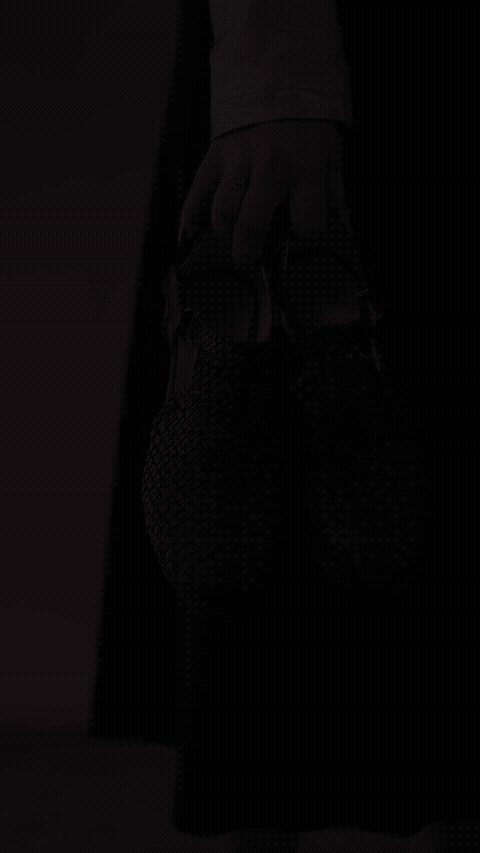Margreet 3cm sandals — Woven shoe held by hand against dark trousers — Scarpe Handmade