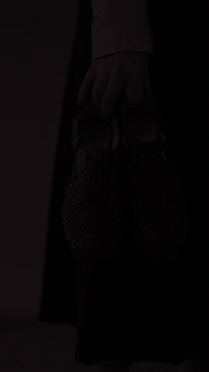Margreet 3cm sandals — Woven shoe held by hand against dark trousers — Scarpe Handmade
